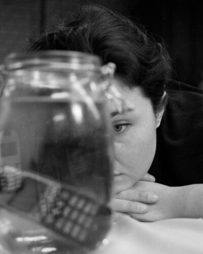 junge Frau blickt in ein Glas mit einem Handy